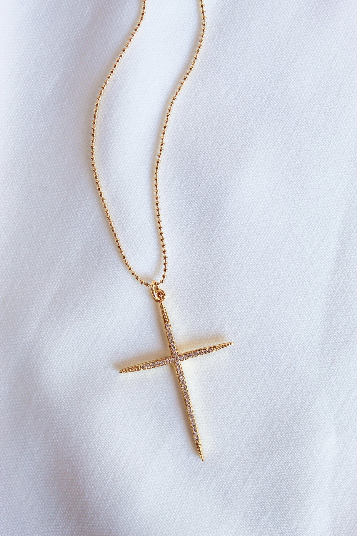 The Meyer Necklace by Kinsey Designs Archives features a gold filled cross pendant with cubic zirconia on a white fabric background. Its delicate 20-inch chain adds elegance to this stylish accessory.