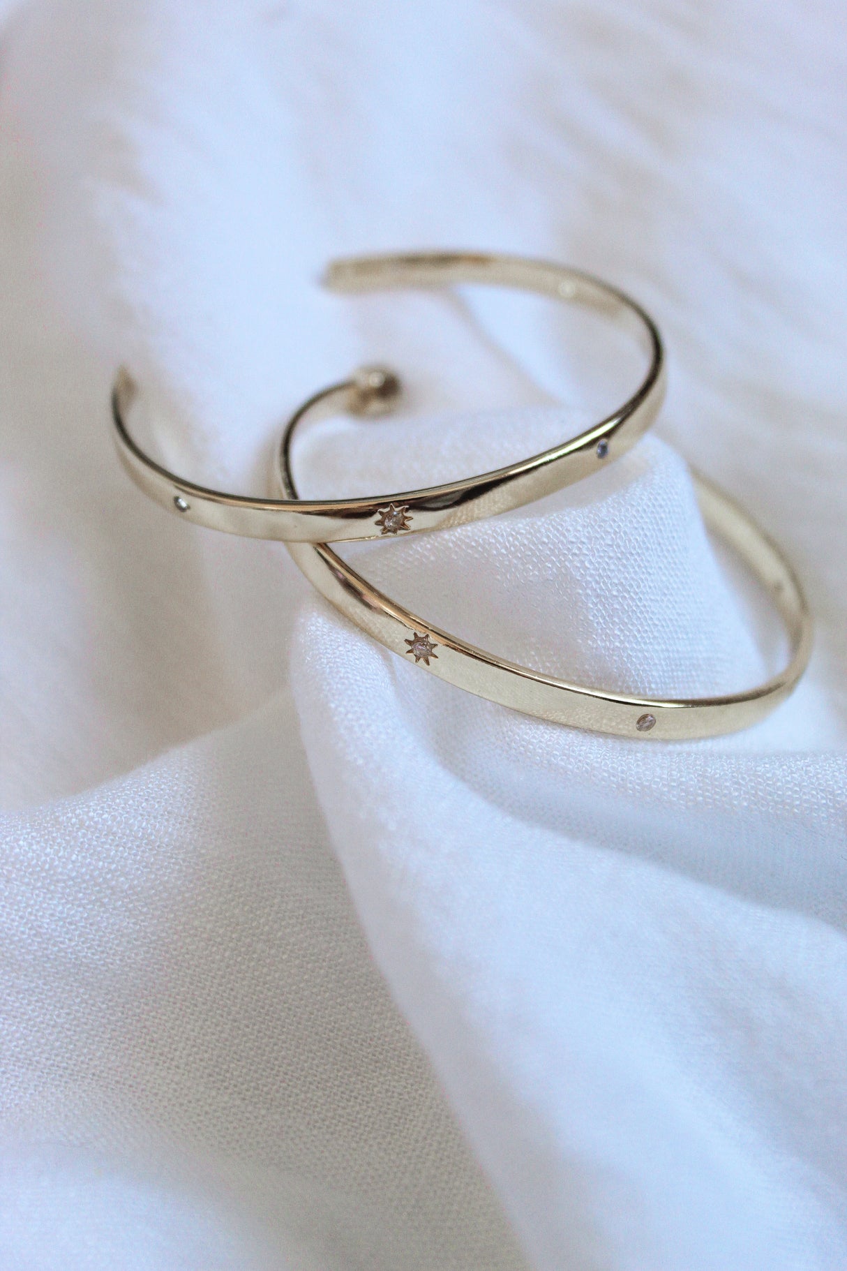 Two gold plated Molly Hoops by Kinsey Designs Archives with delicate star engravings rest on soft white fabric—a radiant duo you'll love from our exclusive Sample Sale.