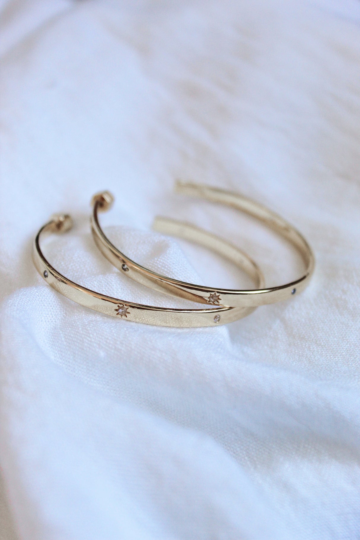 The Molly Hoop by Kinsey Designs Archives—two gold plated bangles with delicate star engravings, displayed on soft white fabric. Discover this elegant piece at our Sample Sale.