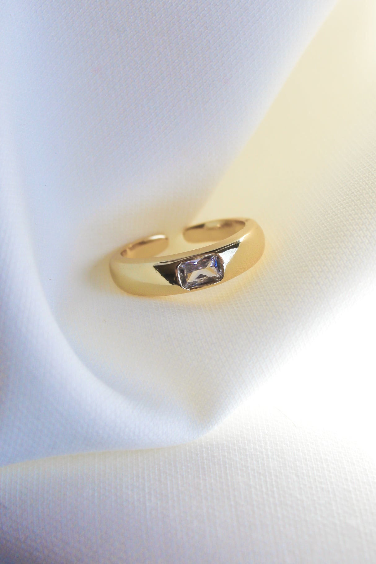 The Preston Ring by Kinsey Designs Archives, featuring a rectangular cubic zirconia and gold plating, is displayed on soft white fabric.