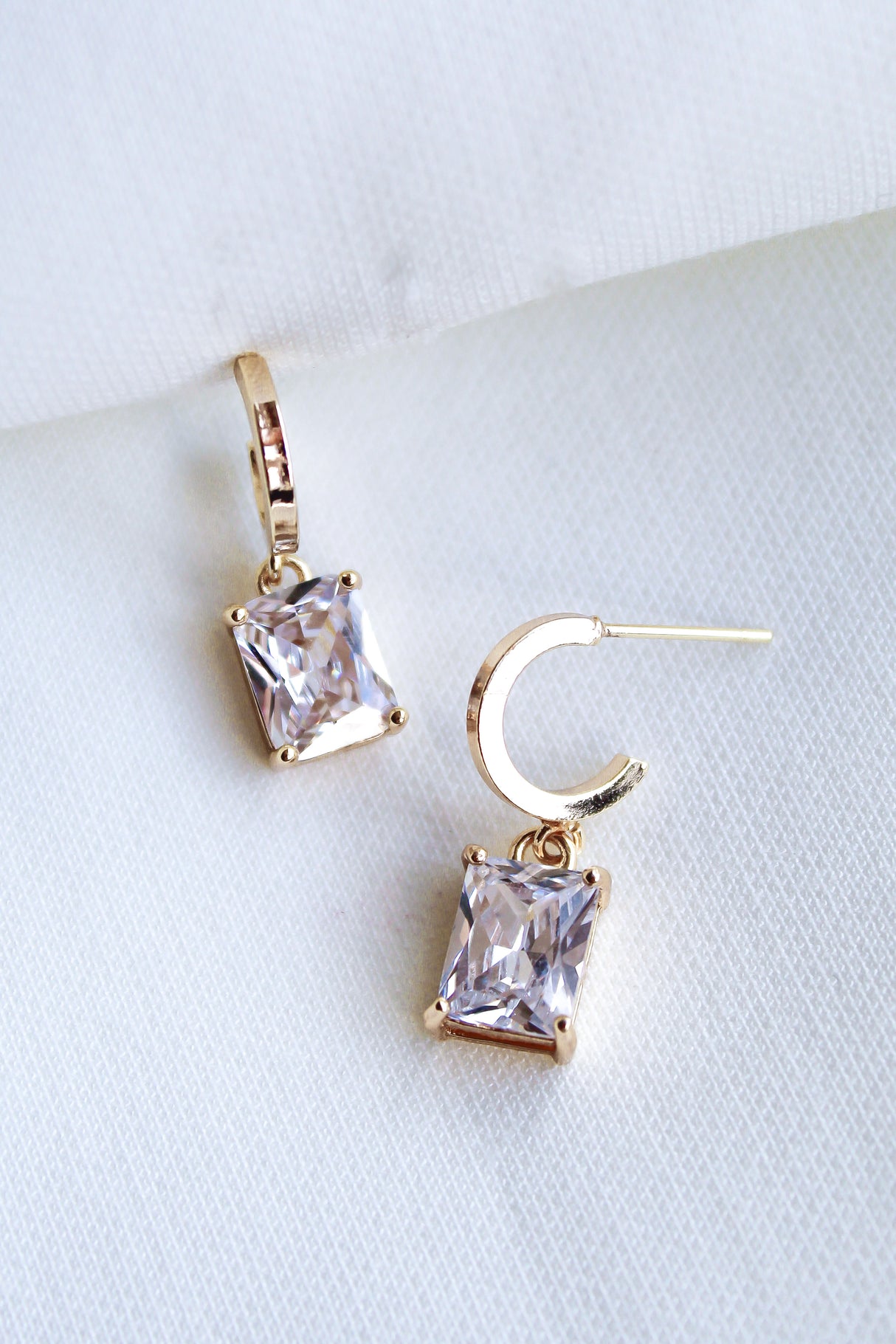 Kinsey Designs Prism Huggies with princess-cut CZ gemstones are shown on a white fabric background.