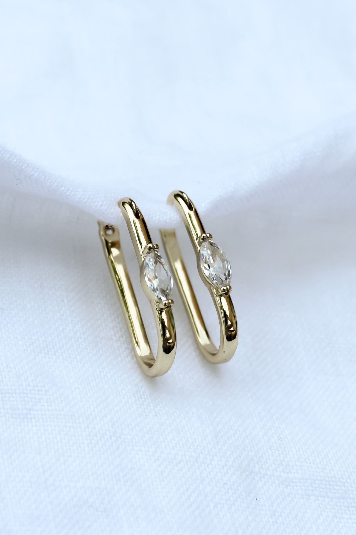The Ragan Huggie by Kinsey Designs Archives features 1" gold filled hoops with oval clear cubic zirconia, displayed on white fabric.