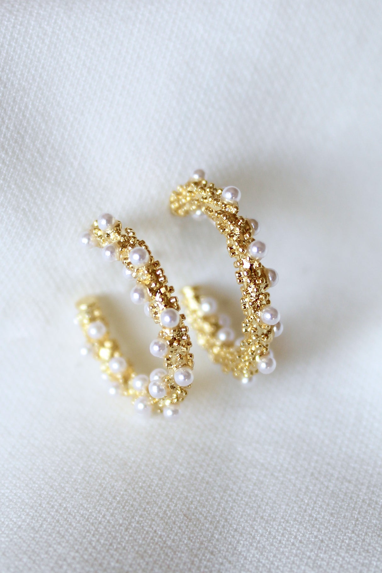 The Reef Hoop by Kinsey Designs Archives features gold hoops with small white pearls, 2" in diameter, displayed on a soft white fabric background.