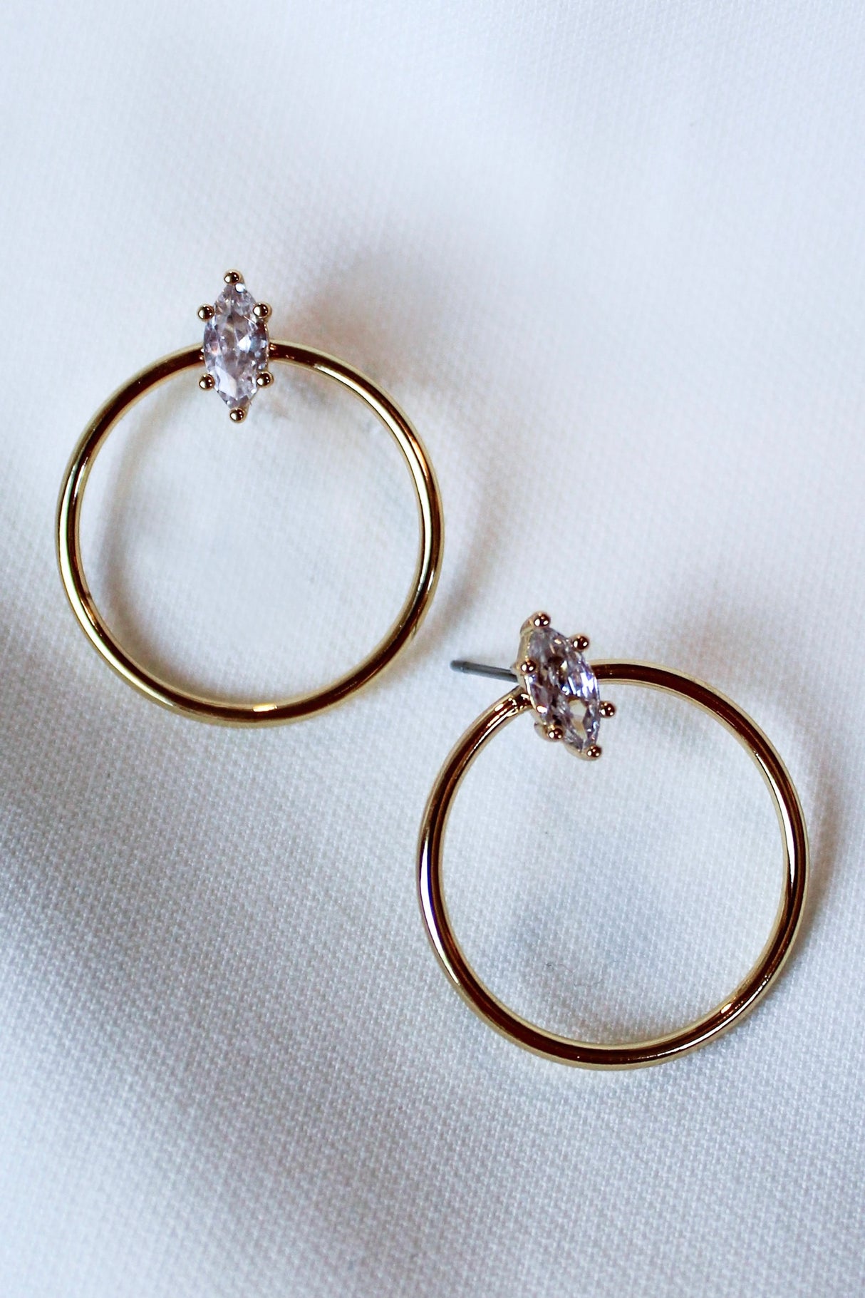 The Remi Hoop by Kinsey Designs Archives features 14K gold plating and marquise-cut cubic zirconia stones. These 1” diameter hoop earrings are shown on a white fabric background.