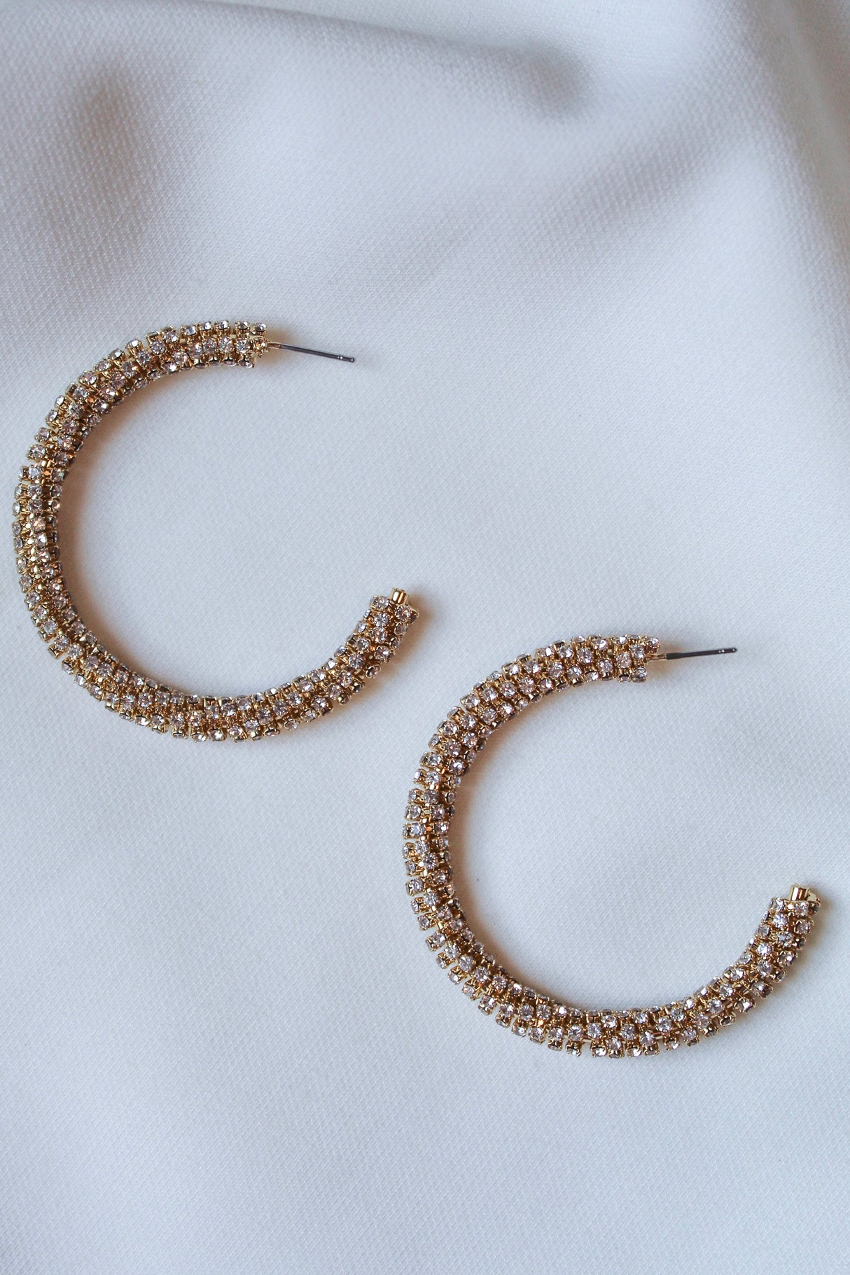 The Kinsey Designs Riley Hoop features gold-plated hoops with embedded cubic zirconia, displayed on a white fabric background—an ideal sample sale find.