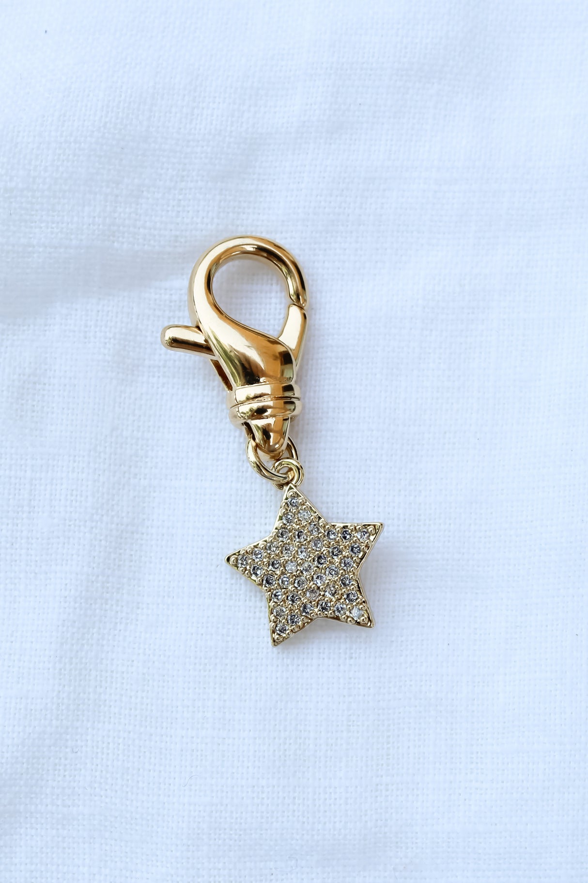 The Star Shoe Charm by Kinsey Designs Archives features a gold-filled clasp with a small, glittery star, displayed on white fabric. Ideal for sample sales or final sale collections.
