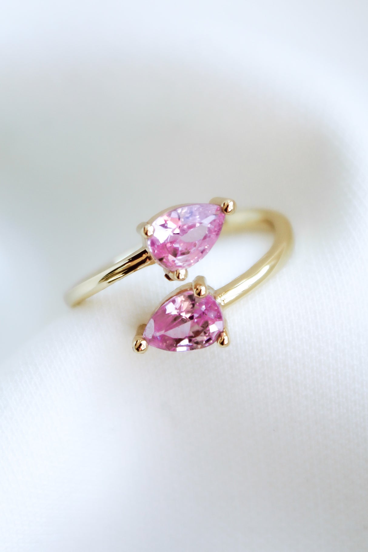 The Teara Ring Pink Ice by Kinsey Designs Archives features two pear-shaped pink cubic zirconia stones, beautifully displayed on a soft white fabric background.