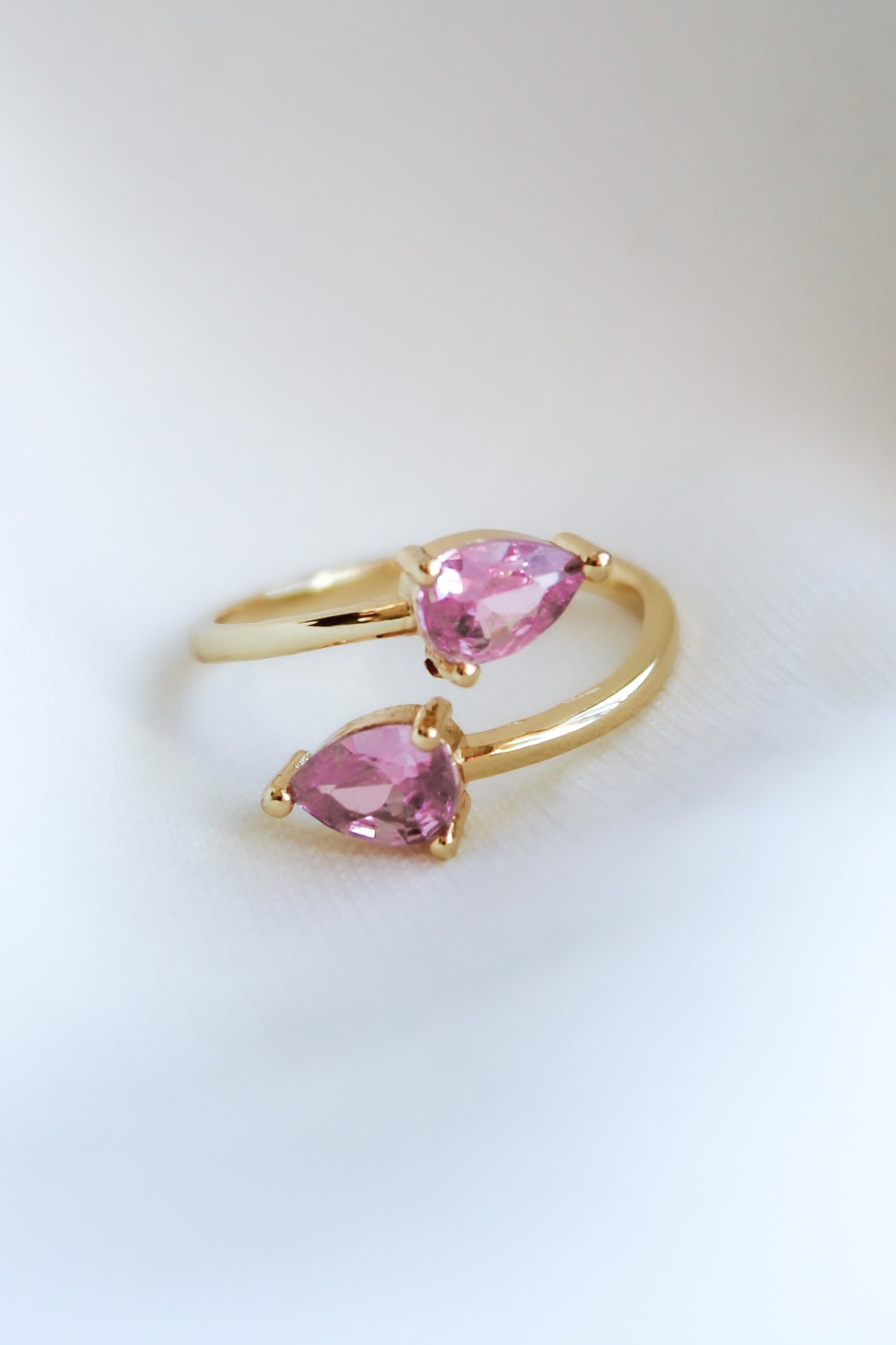 The Teara Ring Pink Ice by Kinsey Designs Archives, featuring two pear-shaped pink cubic zirconia stones, sparkles against a soft white background.