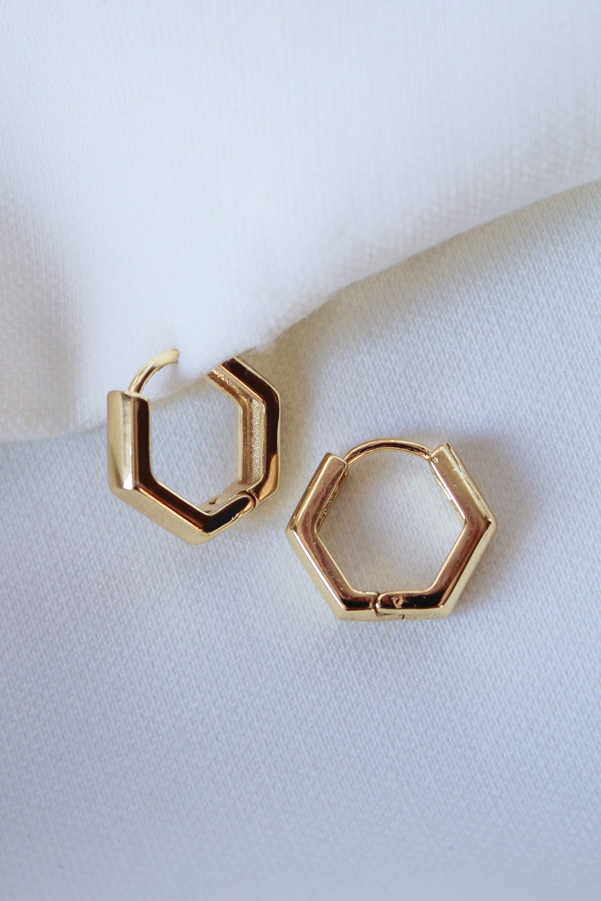 The Theo Hoop by Kinsey Designs Archives—gold filled, hexagon-shaped earrings—rests on white fabric. A modern touch for any look, these earrings are part of our final sale.