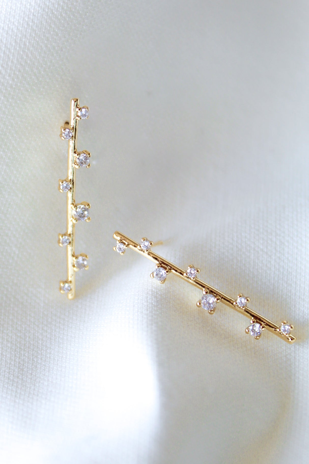 The Walker Earring by Kinsey Designs Archives features a sleek bar design with sparkling cubic zirconia, displayed on soft white satin fabric.