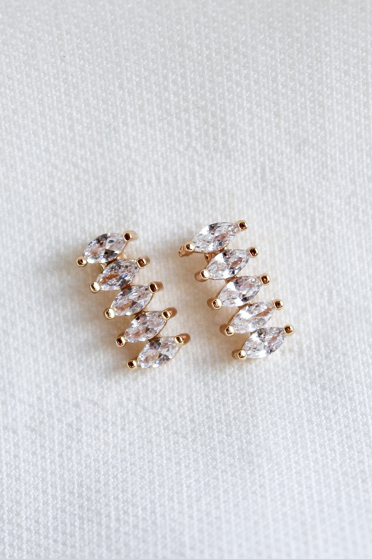 The Winnie Post earrings by Kinsey Designs Archives feature five marquise-cut cubic zirconia stones each, set in gold fill and displayed on a white textured fabric background.