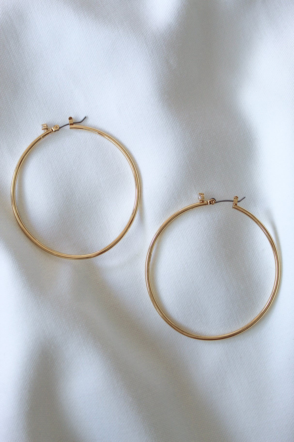 The Xandra Hoop earrings by Kinsey Designs Archives, crafted from gold plated brass, rest elegantly on a soft white fabric background.
