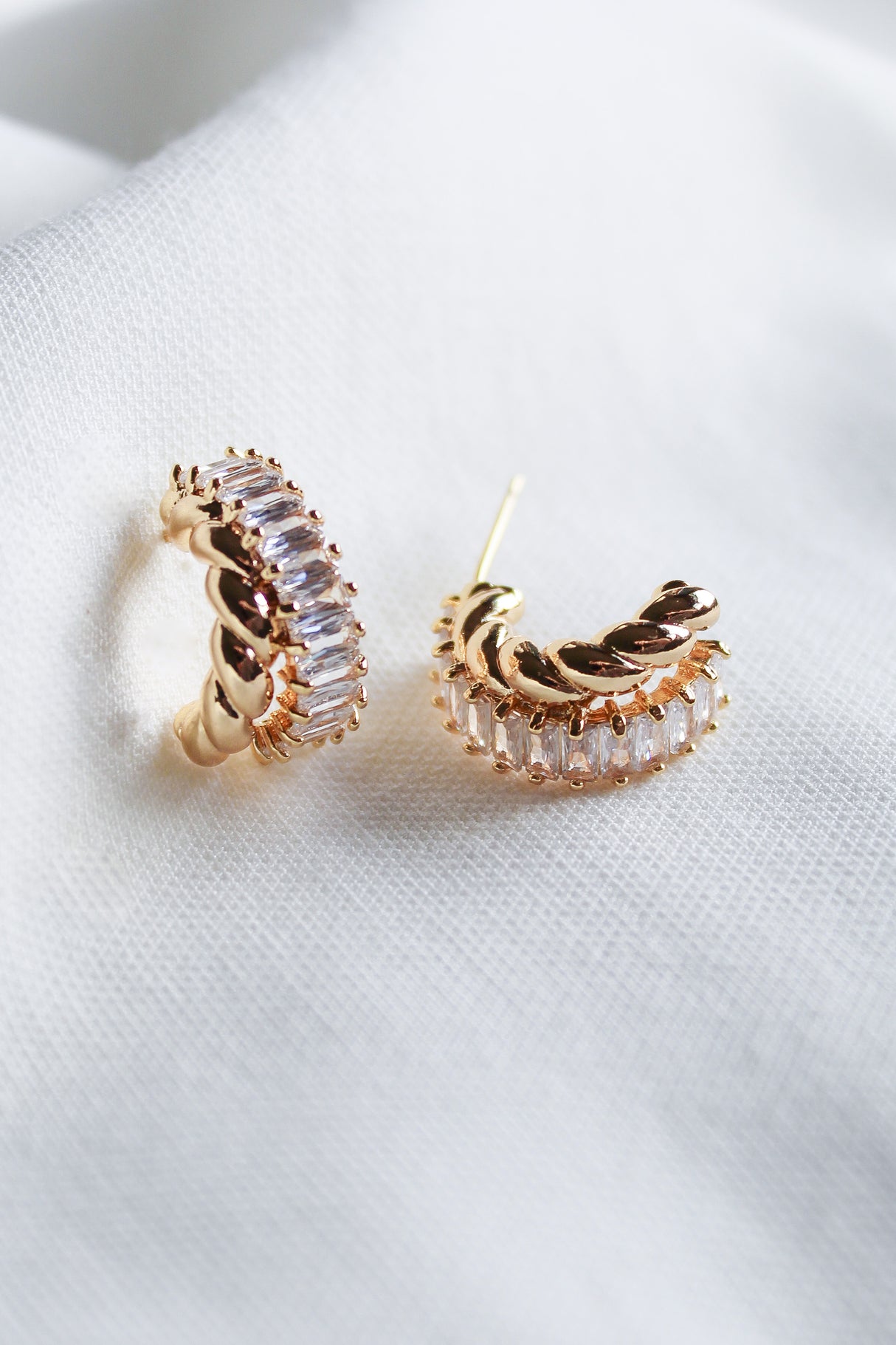 The Zuri Hoop by Kinsey Designs features gold filled earrings accented with clear cubic zirconia, elegantly presented on a soft white fabric background.