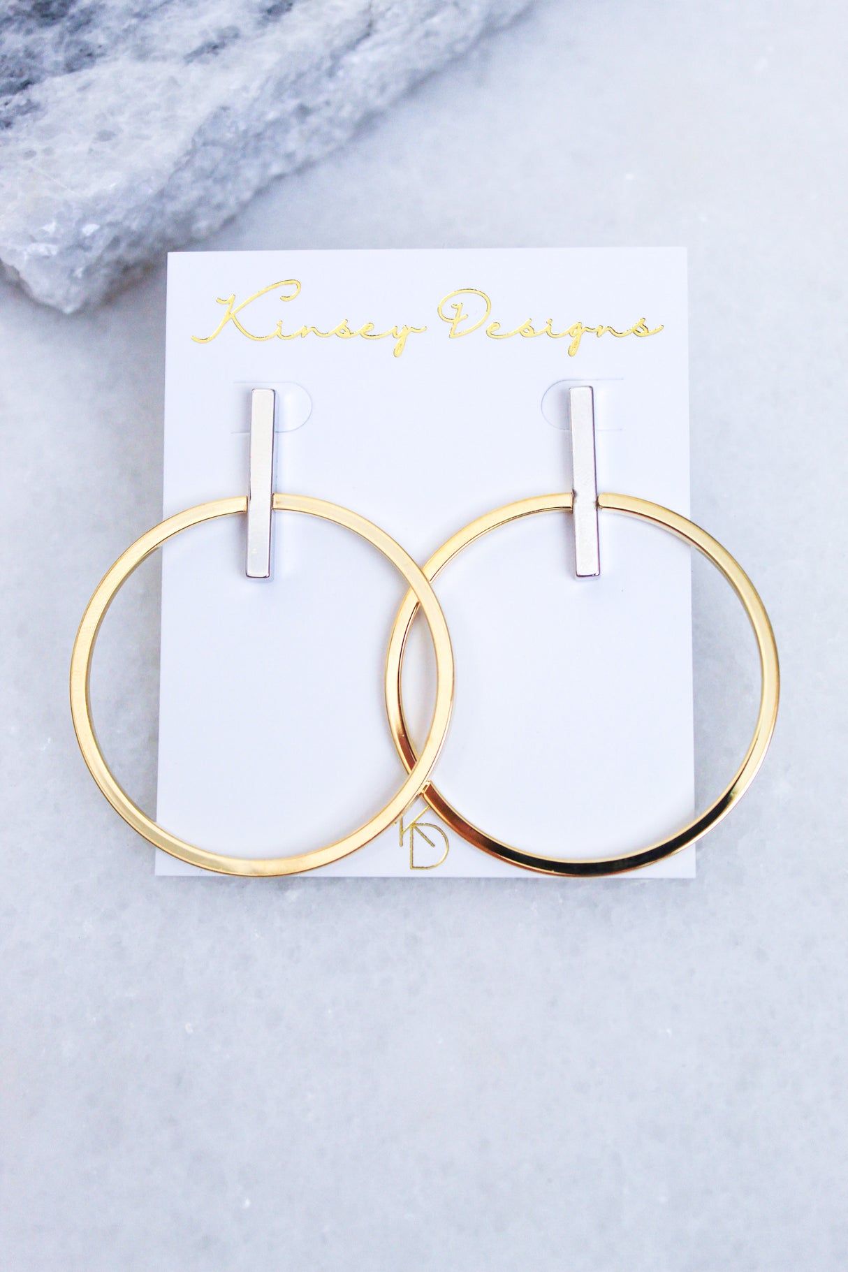 Jocelyn - Mixed Metals gold plated hoop earrings with silver bars (2.5”L x 2”W) by Kinsey Designs Archives, shown on a branded white card atop marble.