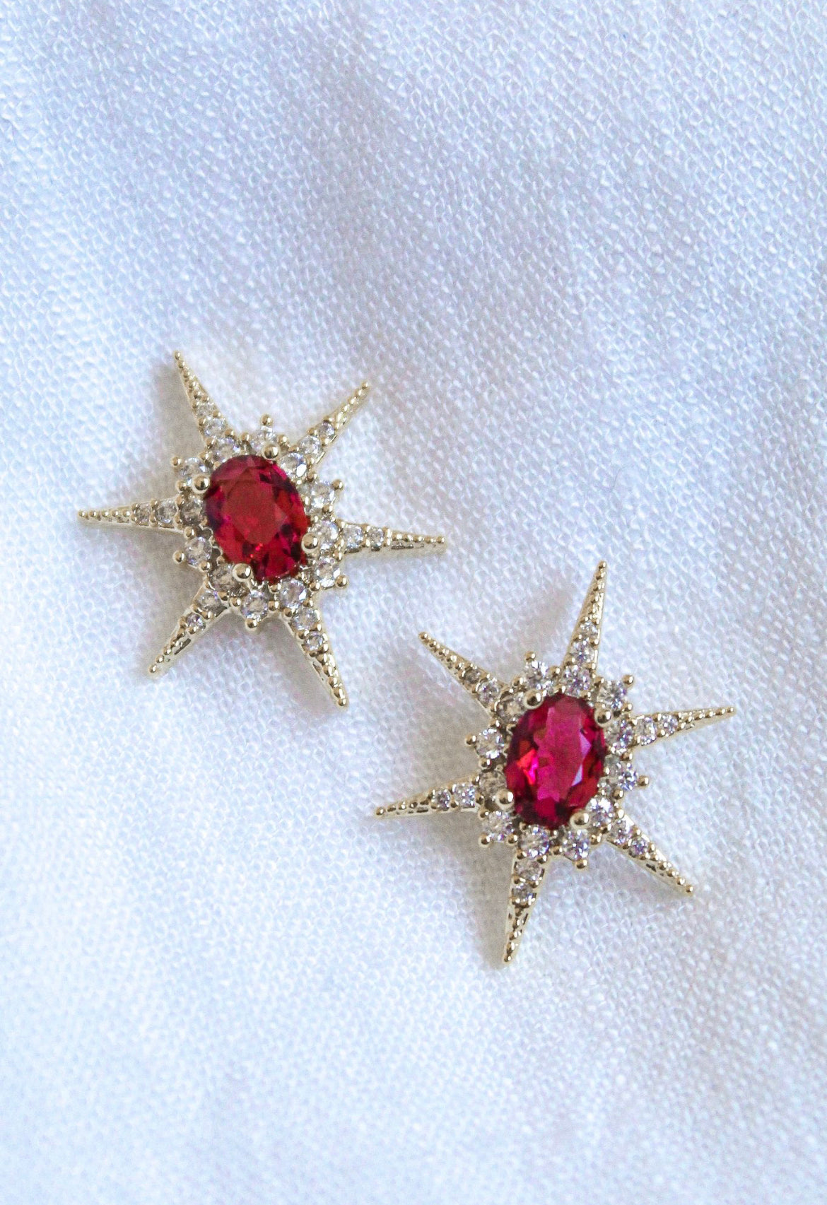 Faye Stud star-shaped earrings by Kinsey Designs feature gold-filled design, red center stones, and cubic zirconia accents. Shown on white fabric—add sparkle to your look! Shop now at our sample sale.