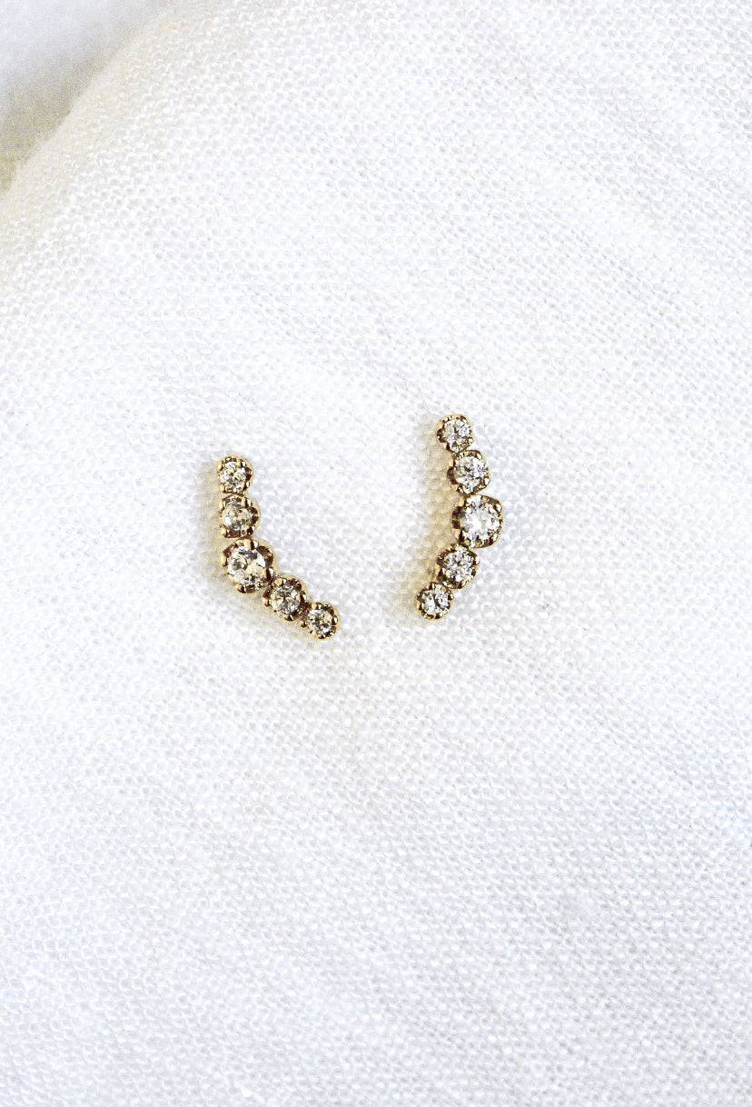 The Always Stud earrings by Kinsey Designs Archives feature a curved, gold-plated design, each 0.5" wide and set with five round diamonds, elegantly displayed on soft white fabric.