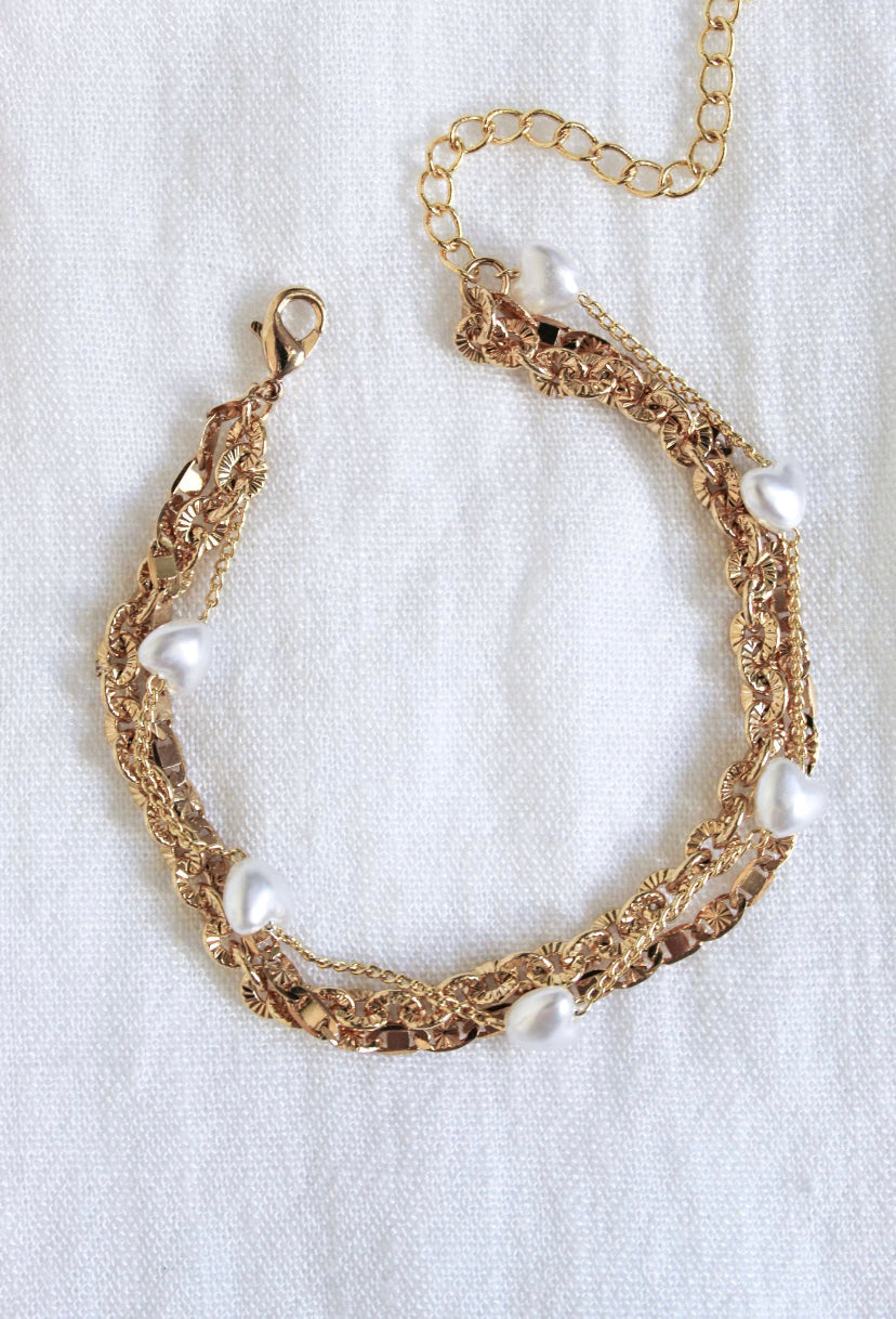 The Beyah Layer Bracelet by Kinsey Designs Archives features a gold-plated brass chain with white pearls, showcased on a white textured fabric background.