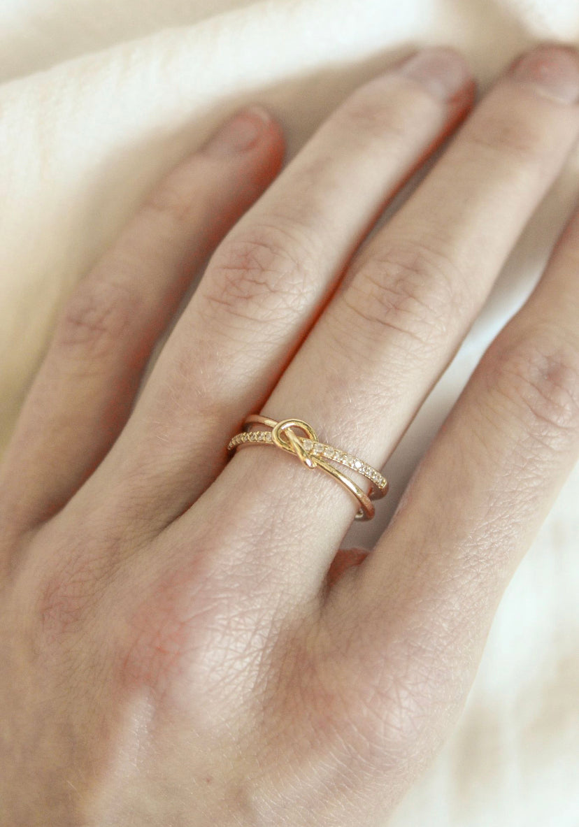 Close-up of a hand wearing two gold rings from Kinsey Designs Archives, including the Knotty Ring—an adjustable gold ring with a knot—paired with a sparkling diamond band; fits sizes 7-9 perfectly.