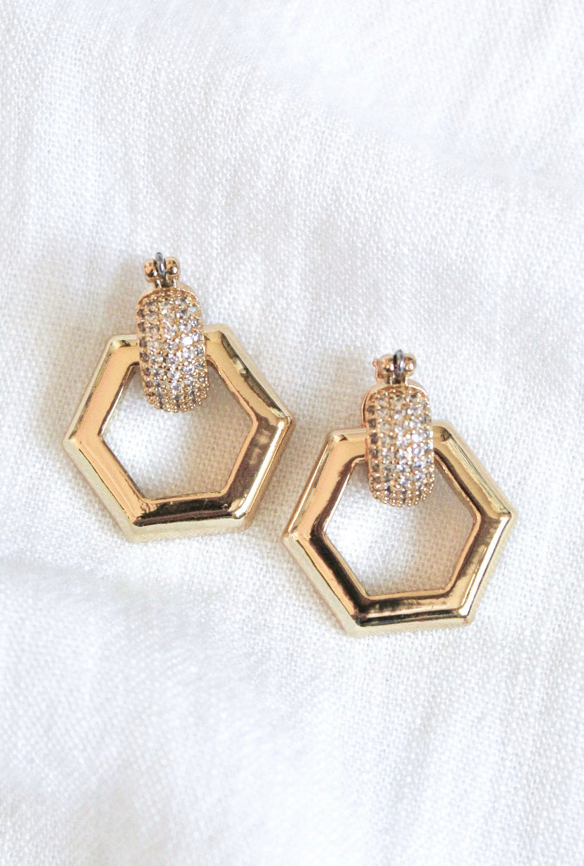 The Stevie 2-Way Hoop by Kinsey Designs Archives features gold-plated huggie earrings with removable hexagon drops and cubic zirconia accents, shown on a white fabric background.