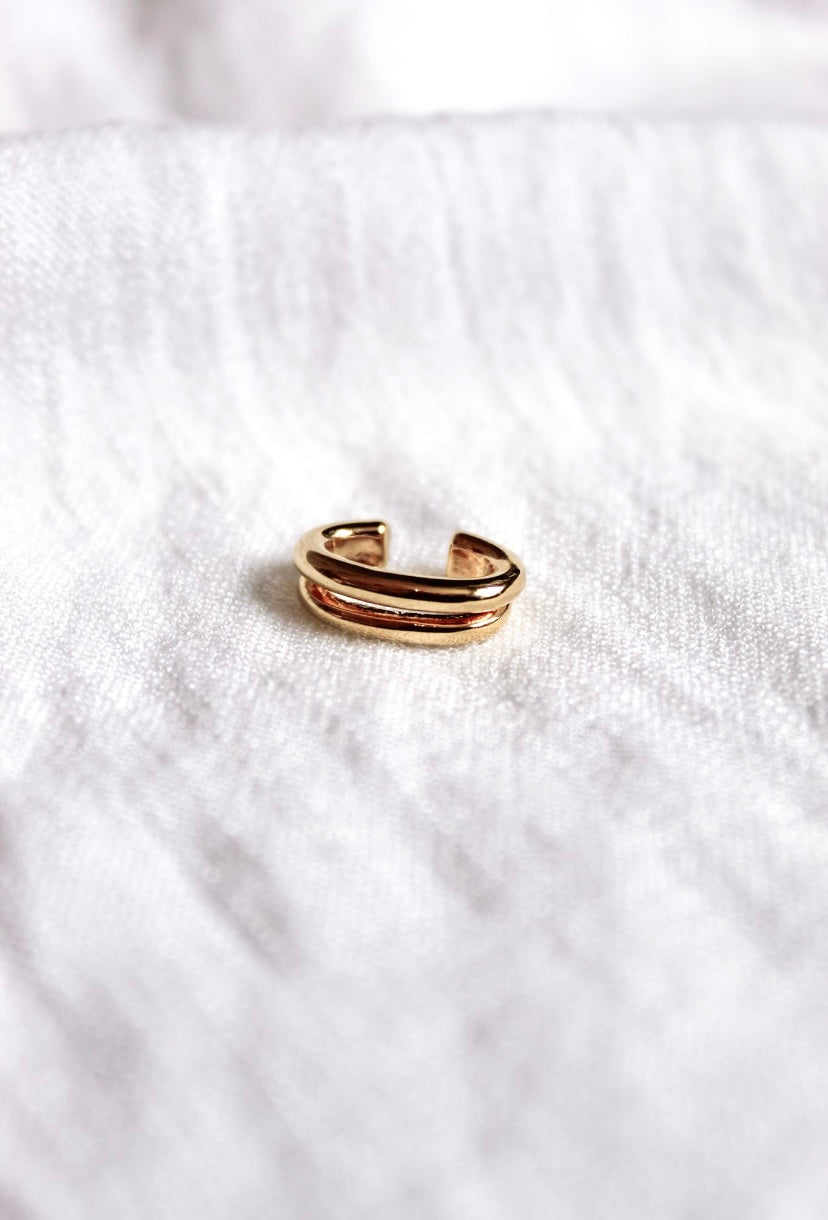 The Blurred Lines Ear Cuff by Kinsey Designs Archives features a gold-plated double band design, measuring .75” wide, shown resting on soft white textured fabric.