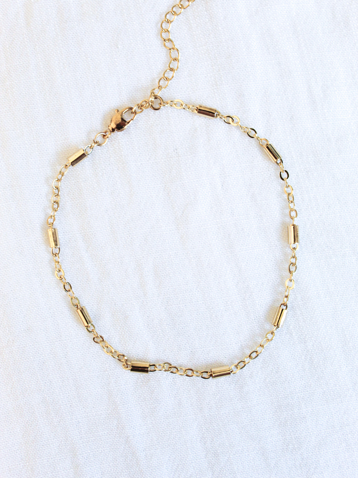 The Azure Anklet - Gold Filled by Kinsey Designs Archives features delicate cylindrical beads, beautifully displayed on a white fabric background.