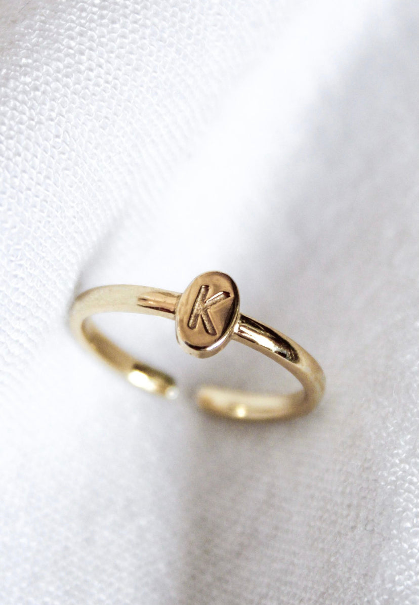The Kinsey Designs Collection's Kinsey Initial Ring Letter K features an oval face engraved with "K," shown resting on white textured fabric.