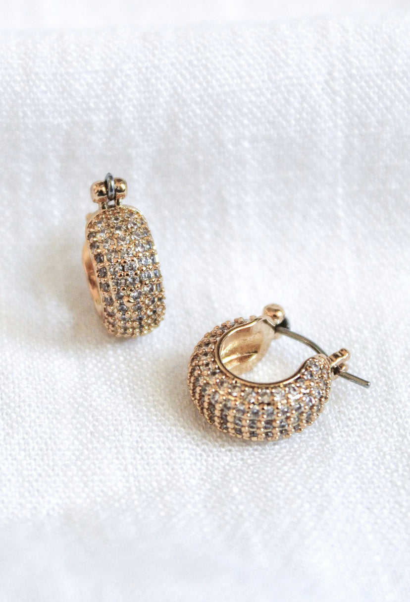 The Stevie 2-Way Hoop by Kinsey Designs Archives features gold-plated huggie hoops adorned with sparkling cubic zirconia, displayed on a white fabric background.