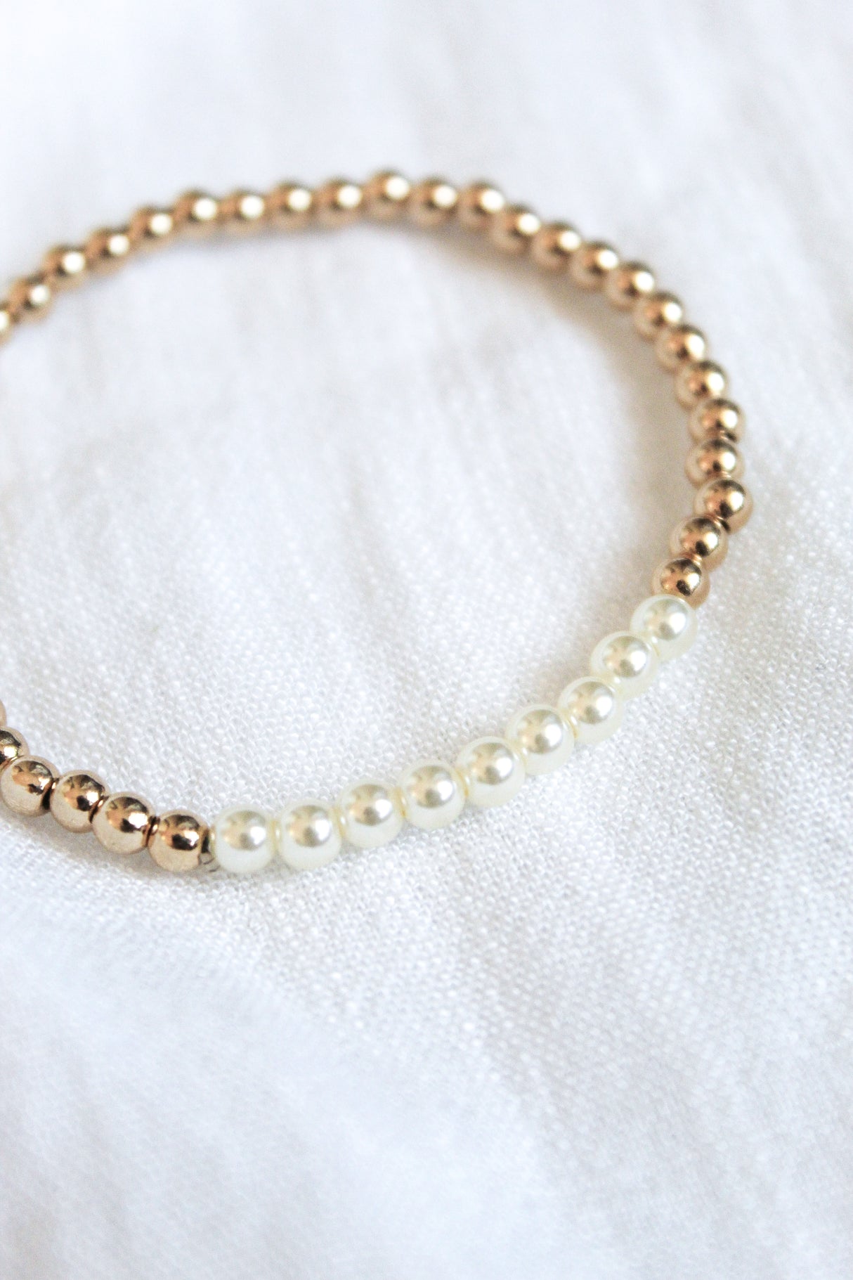 The Liam Stacking Bracelet by Kinsey Designs features gold filled and white pearl beads in an adjustable stretch design, shown on a white fabric background. Available in multiple sizes.