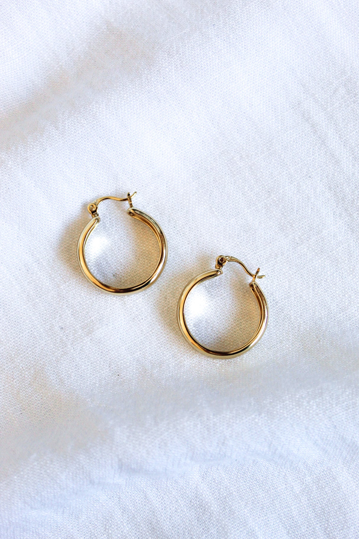 The Doreen earrings by Kinsey Designs Archives are small 14k gold filled hoops, .75 inch wide, displayed on a white fabric background.
