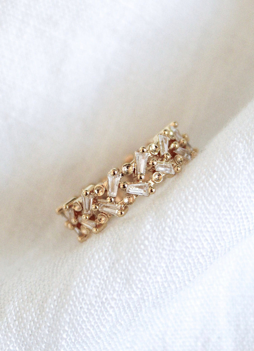 The Rylan Ring by Kinsey Designs Archives features gold plating with baguette and round diamonds, adjustable for a perfect fit, displayed on a soft, white textured fabric background.