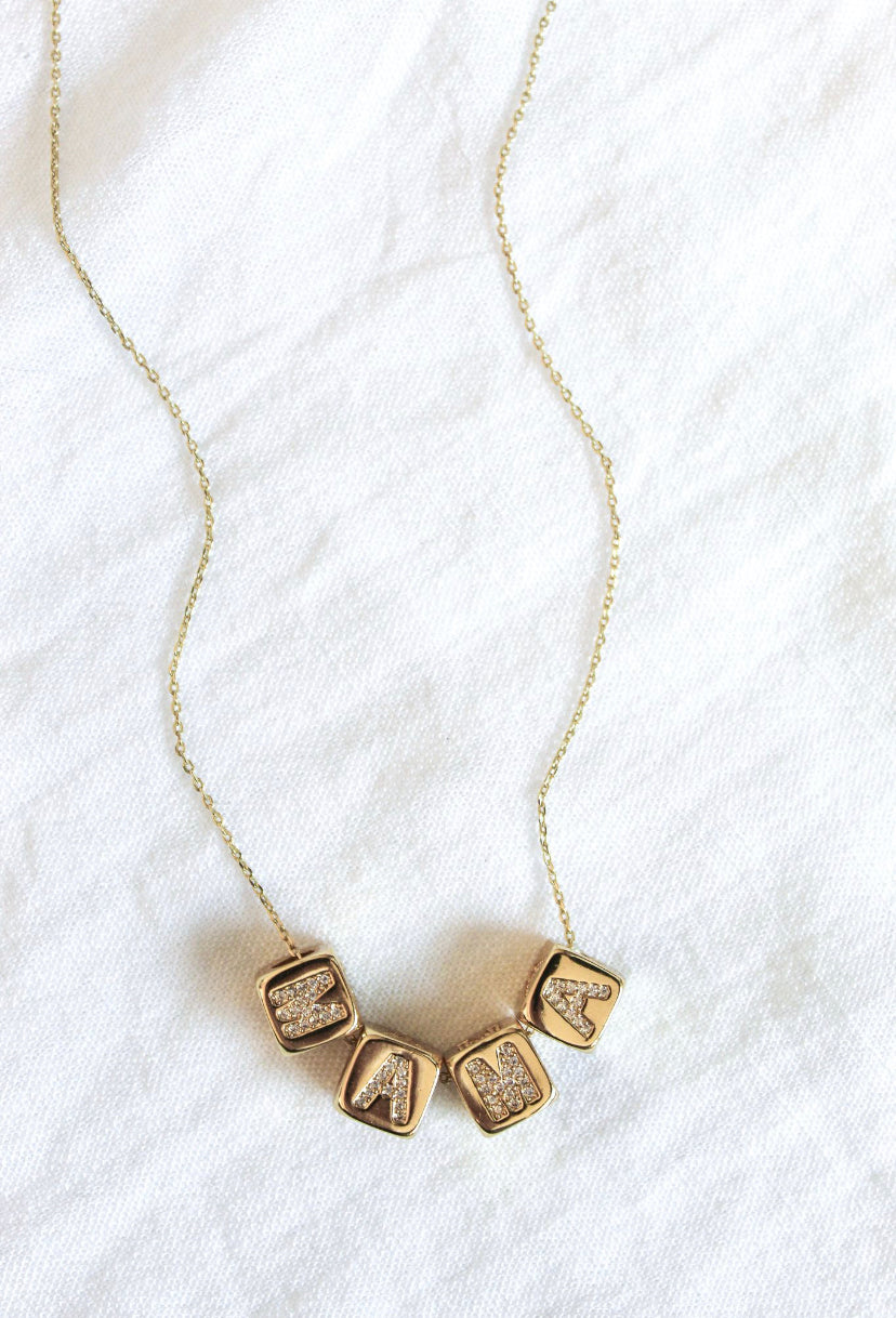 The Kinsey Designs MAMA Block Necklace features four gold cube-shaped letter charms spelling "MAMA"—a perfect Mother's Day gift and a stylish accessory for moms.