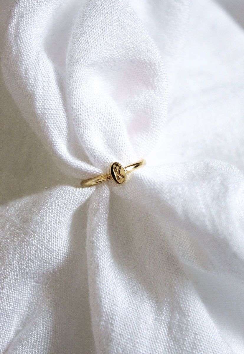 The Kinsey Initial Ring by Kinsey Designs features an engraved letter "K" and rests on soft, white textured fabric—a perfect piece of personalized jewelry.