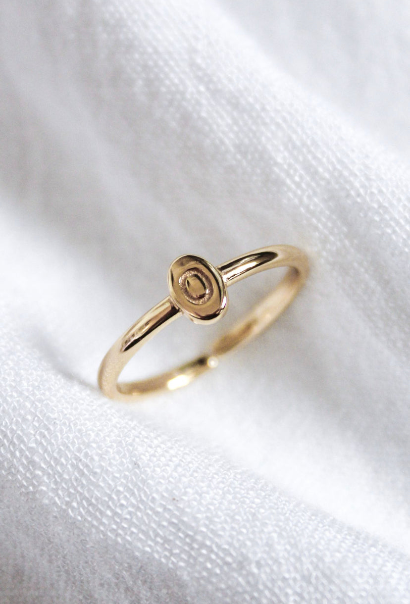 The Kinsey Initial Ring by Kinsey Designs features a small, oval-shaped design and rests on soft white textured fabric—a perfect piece of personalized jewelry.
