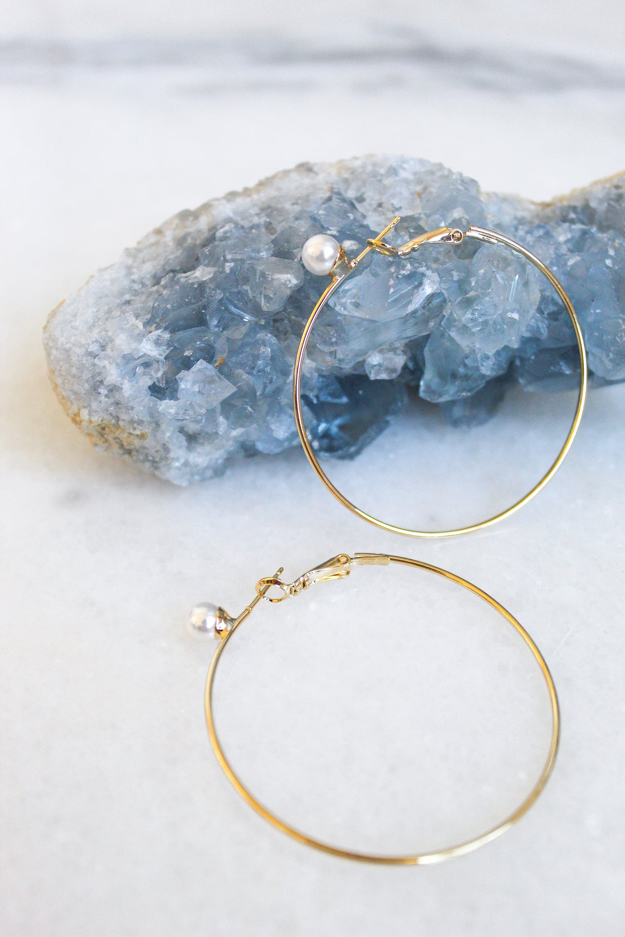 The Ashton Pearl earrings by Kinsey Designs Archives feature freshwater pearl accents on 16K gold-plated hoops, beautifully displayed on raw blue crystal against a white background—an ideal summer jewelry addition.