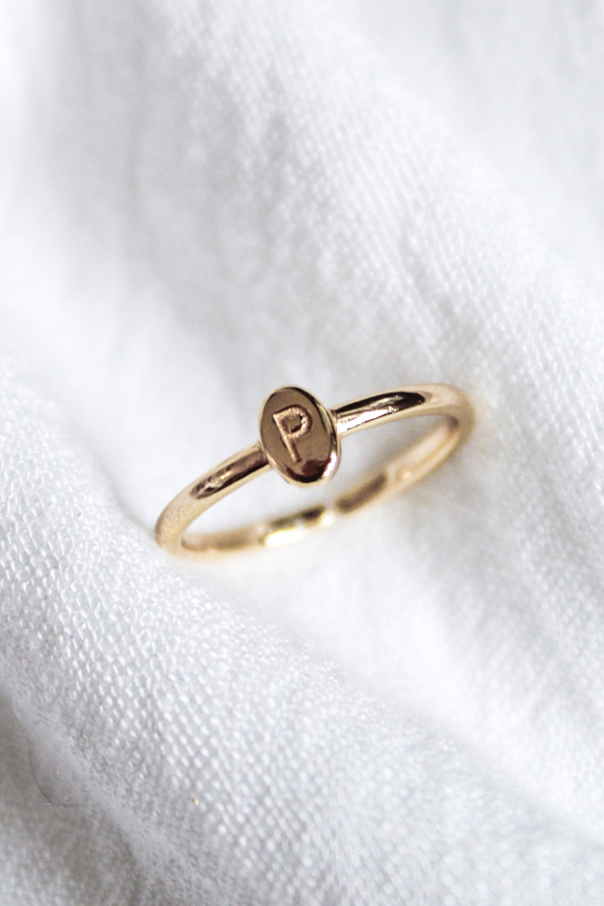 The Kinsey Designs Collection Kinsey Initial Ring with a small oval face engraved with the letter "P" is displayed on white fabric.