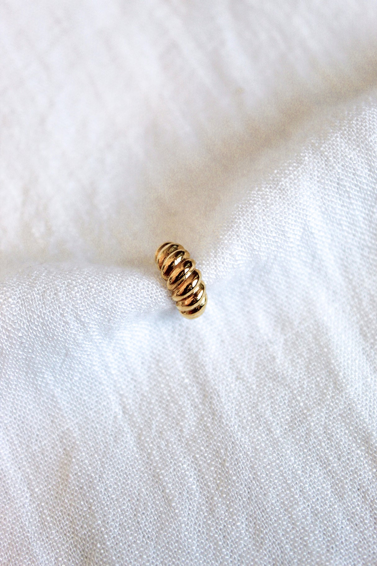 The Metz Cuff by Kinsey Designs Archives, a small gold-plated ridged piece, rests on soft white textured fabric.