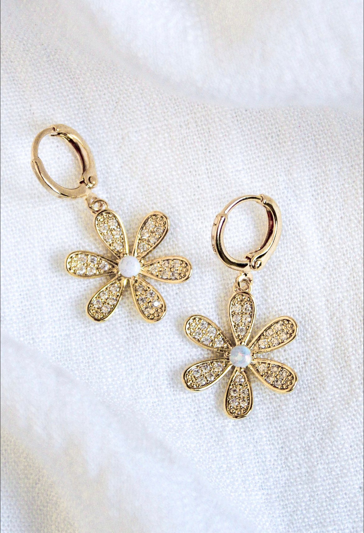 The Sandi Huggie by Kinsey Designs Archives features 16k gold plating, flower shapes with crystal petals and pearl centers, displayed on a white fabric background.