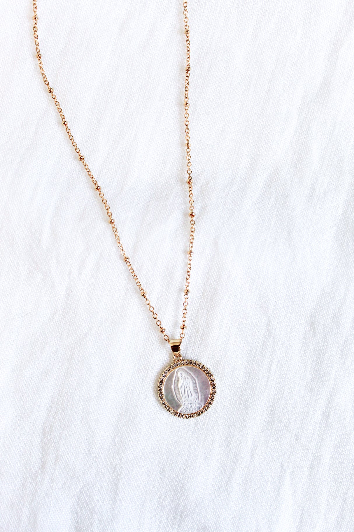 The Alivia necklace by Kinsey Designs Archives features an engraved oval pendant and a mother of pearl charm, shown on a white fabric background.
