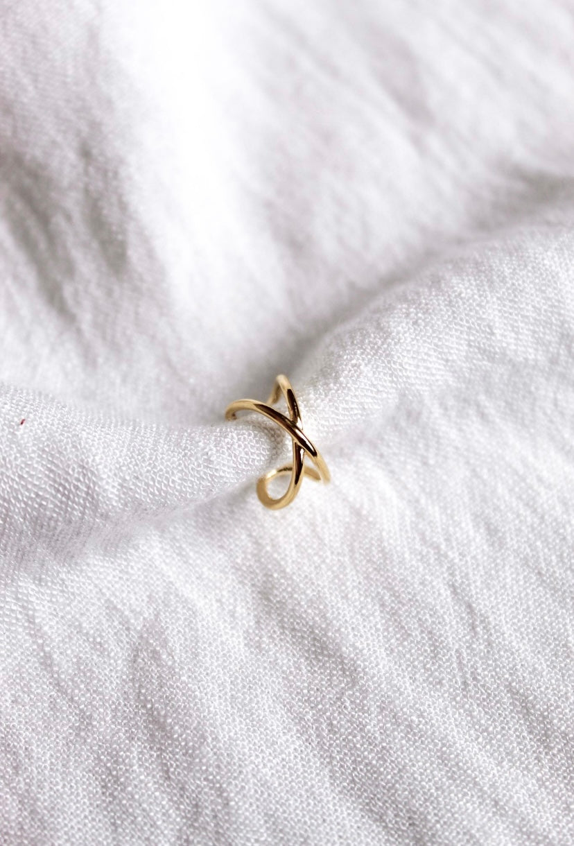 The Criss-Cross Ear Cuff from Kinsey Designs Archives, gold plated with a .5" circumference, rests on soft, white textured fabric.