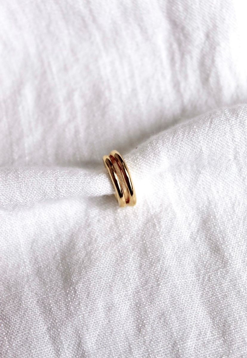 The Blurred Lines Ear Cuff by Kinsey Designs Archives, a small gold-plated double-band ear cuff, .75” wide, is displayed resting on white textured fabric.
