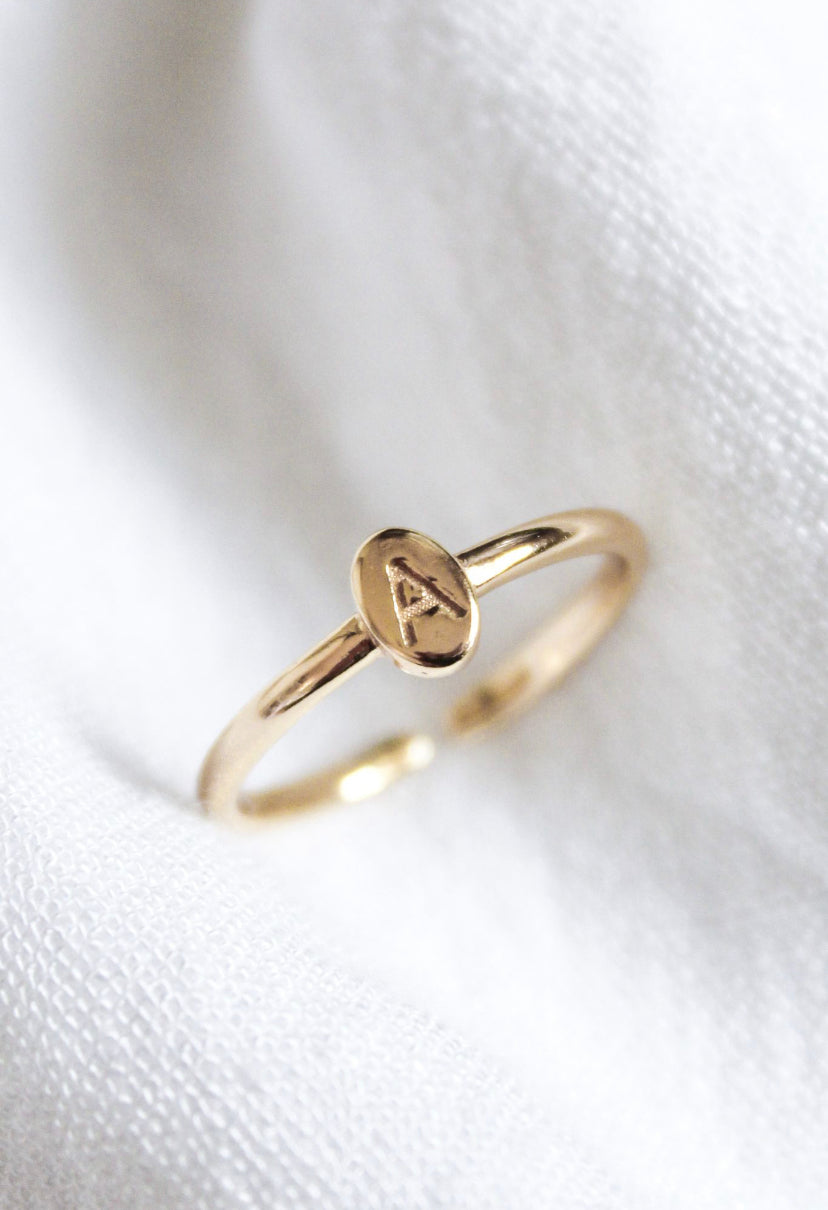 The Kinsey Initial Ring Letter A from the Kinsey Designs Collection features an engraved "A" on an oval gold face, showcased on white textured fabric.
