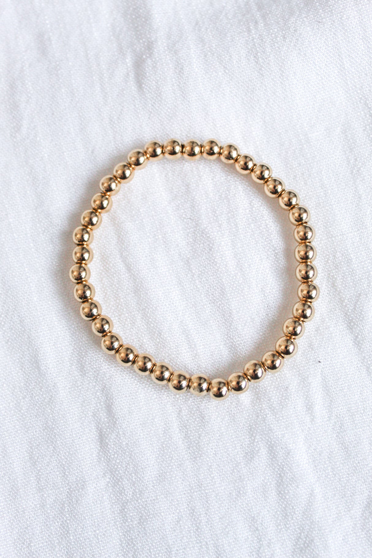 The Liam Stacking Bracelet by Kinsey Designs, shown in a circle on white fabric, features an adjustable stretch design and is available in multiple sizes.