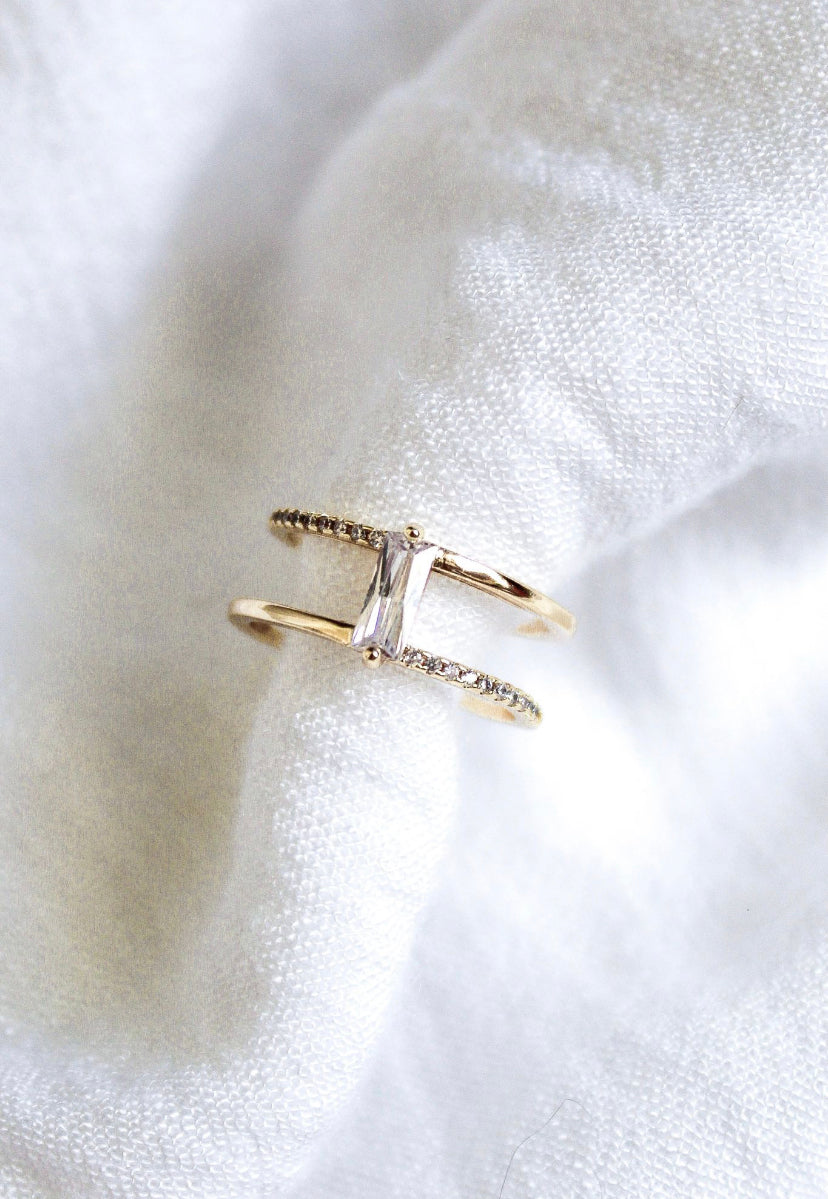 The Cora Ring by Kinsey Designs is an elegant open ring showcasing a rectangular baguette CZ center stone with sparkling side accents, beautifully presented on soft white fabric.