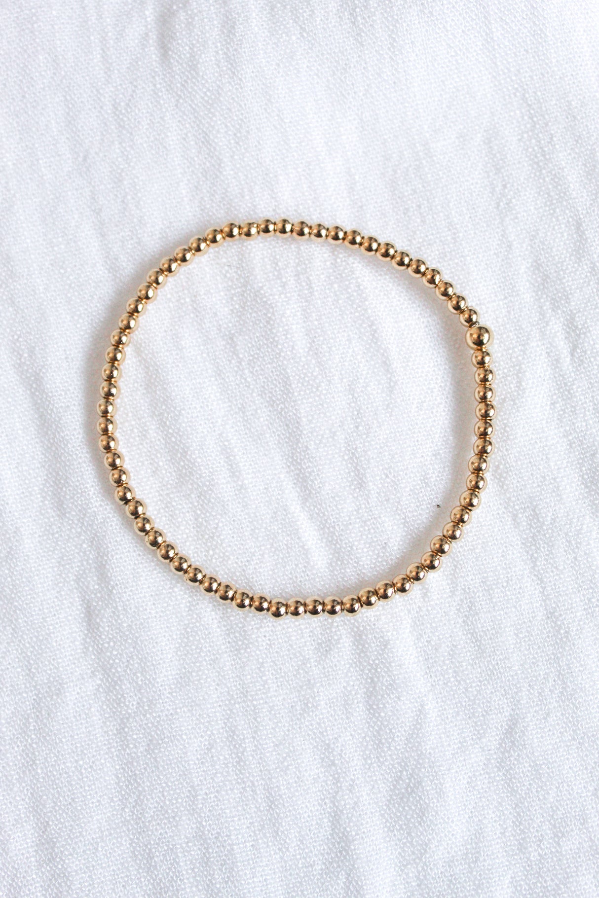 The Liam Stacking Bracelet by Kinsey Designs, shown in a circle on white textured fabric, features gold-filled beads and an adjustable stretch design for a comfortable fit. Available in multiple sizes.