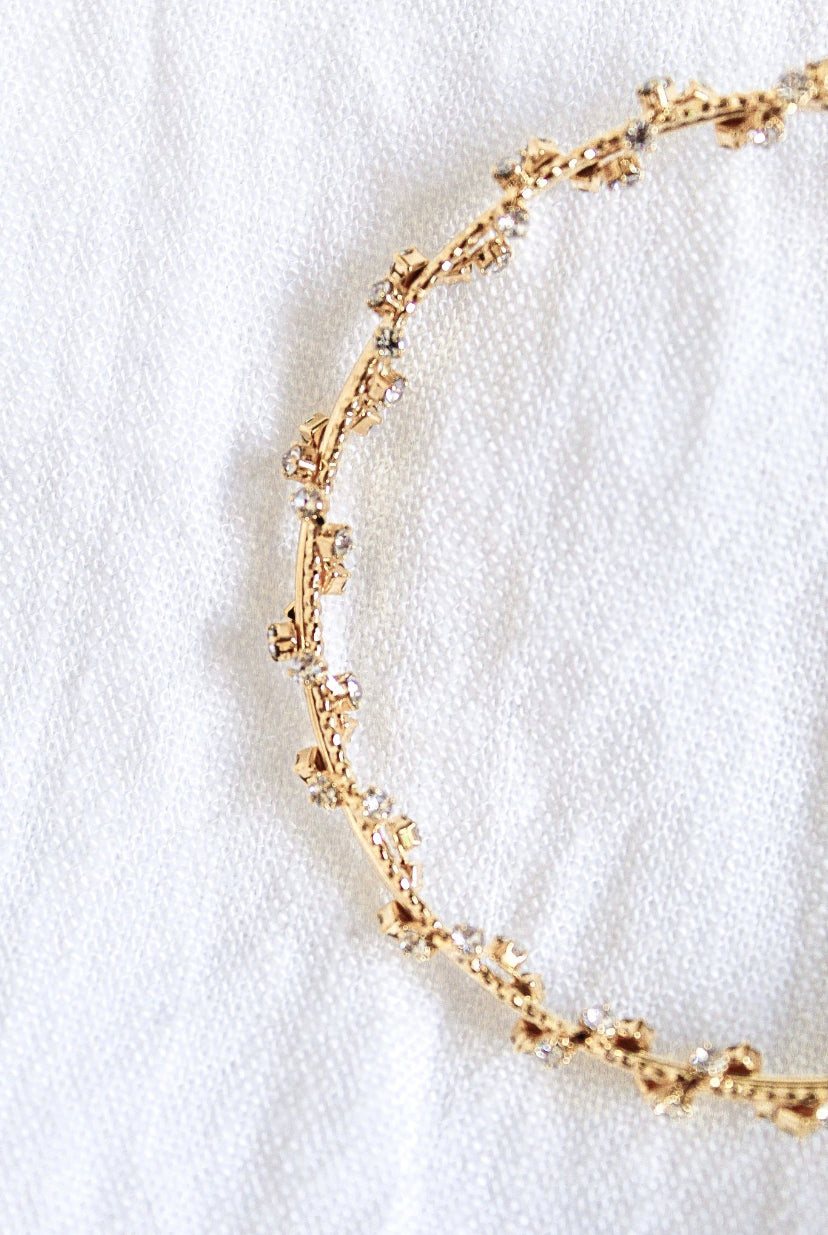 The Staci Hoop by Kinsey Designs Archives, featuring gold plating and delicate cubic zirconia crystals, is displayed on a soft white textured fabric background.