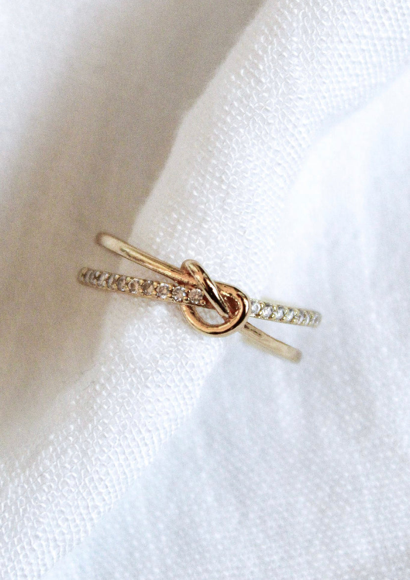The Knotty Ring by Kinsey Designs Archives is a gold-plated adjustable ring with a gemstone band, fitting sizes 7-9. Shown here on white textured fabric.