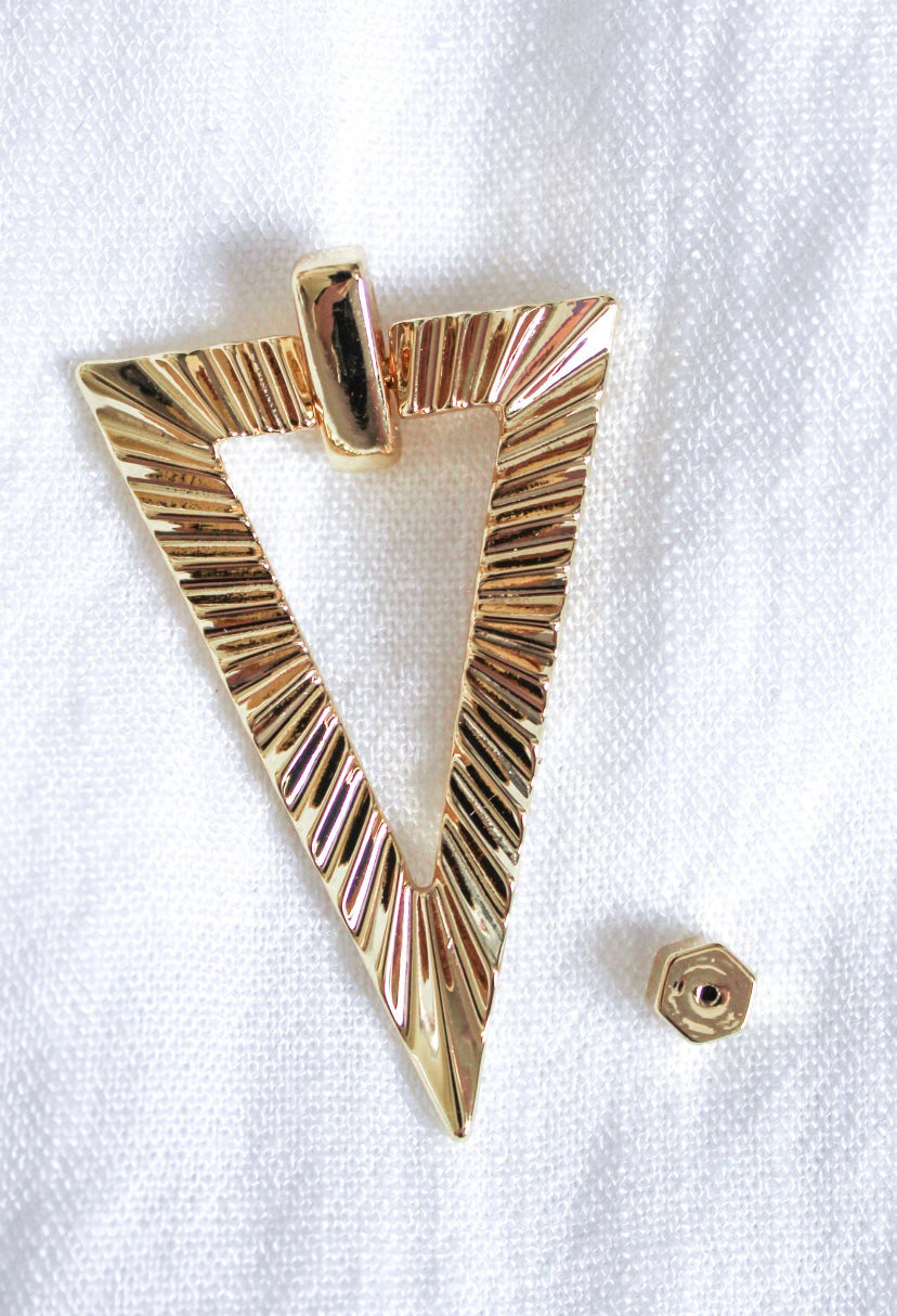 The Colin Earring by Kinsey Designs features a gold triangular pendant with a ridged design and a small hexagonal nut, displayed on white textured fabric. Part of our final sale—pair it with your favorite gold-filled earrings!.
