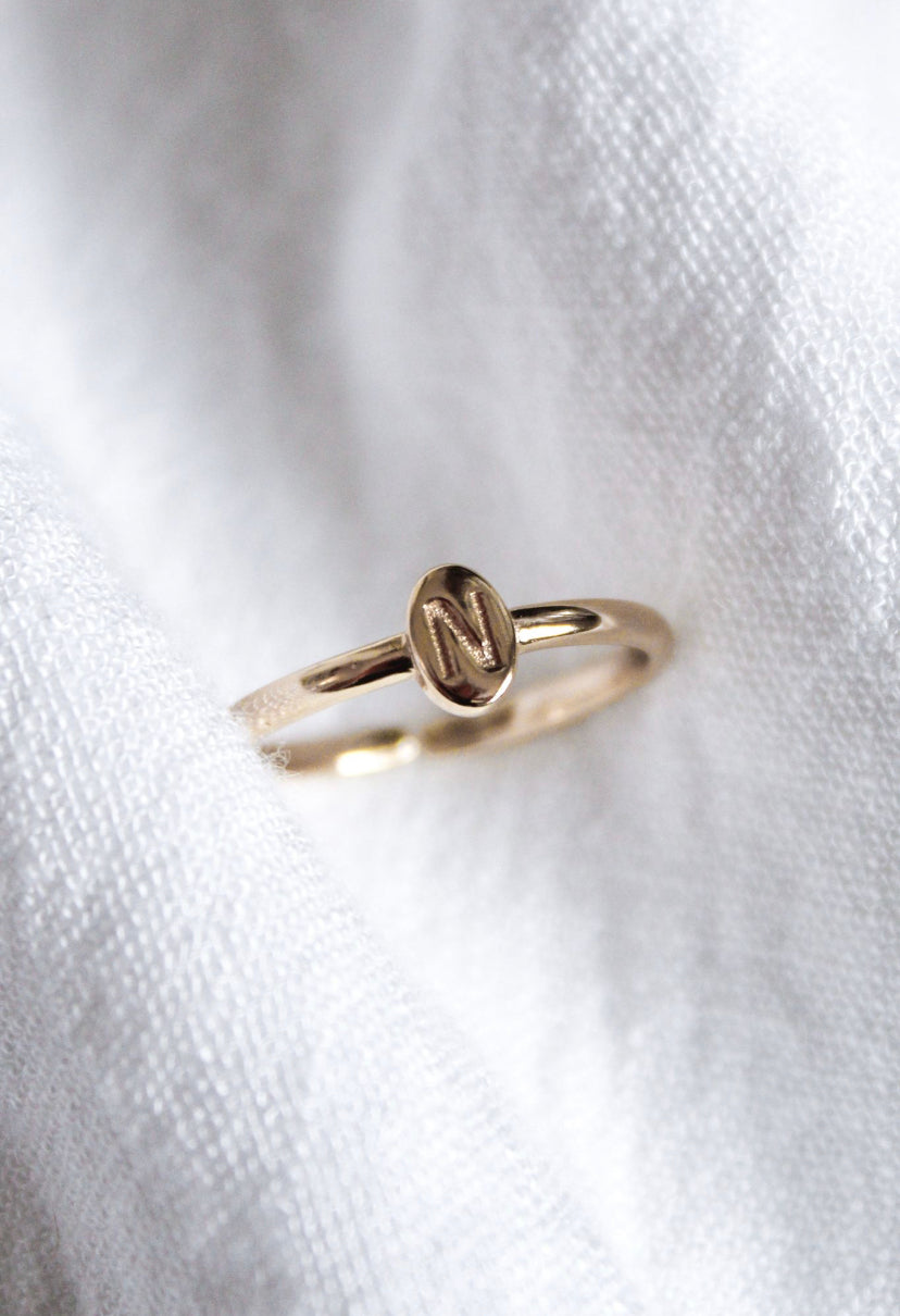 The Kinsey Initial Ring Letter N from the Kinsey Designs Collection features a gold ring with a round plate engraved with the letter "N," shown resting on white fabric.