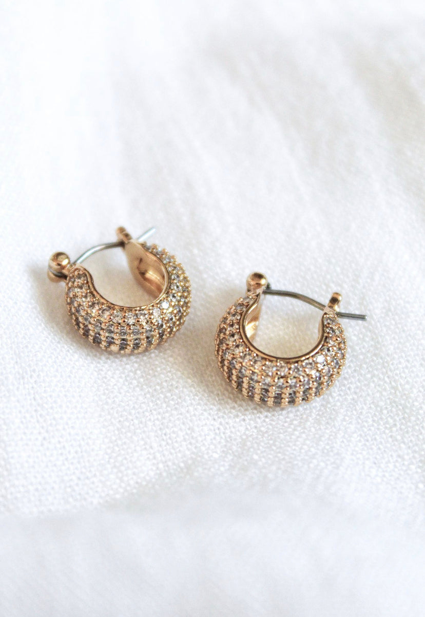 The Stevie 2-Way Hoop by Kinsey Designs Archives features gold-plated huggie hoops with small clear cubic zirconia crystals, shown on a white fabric background.