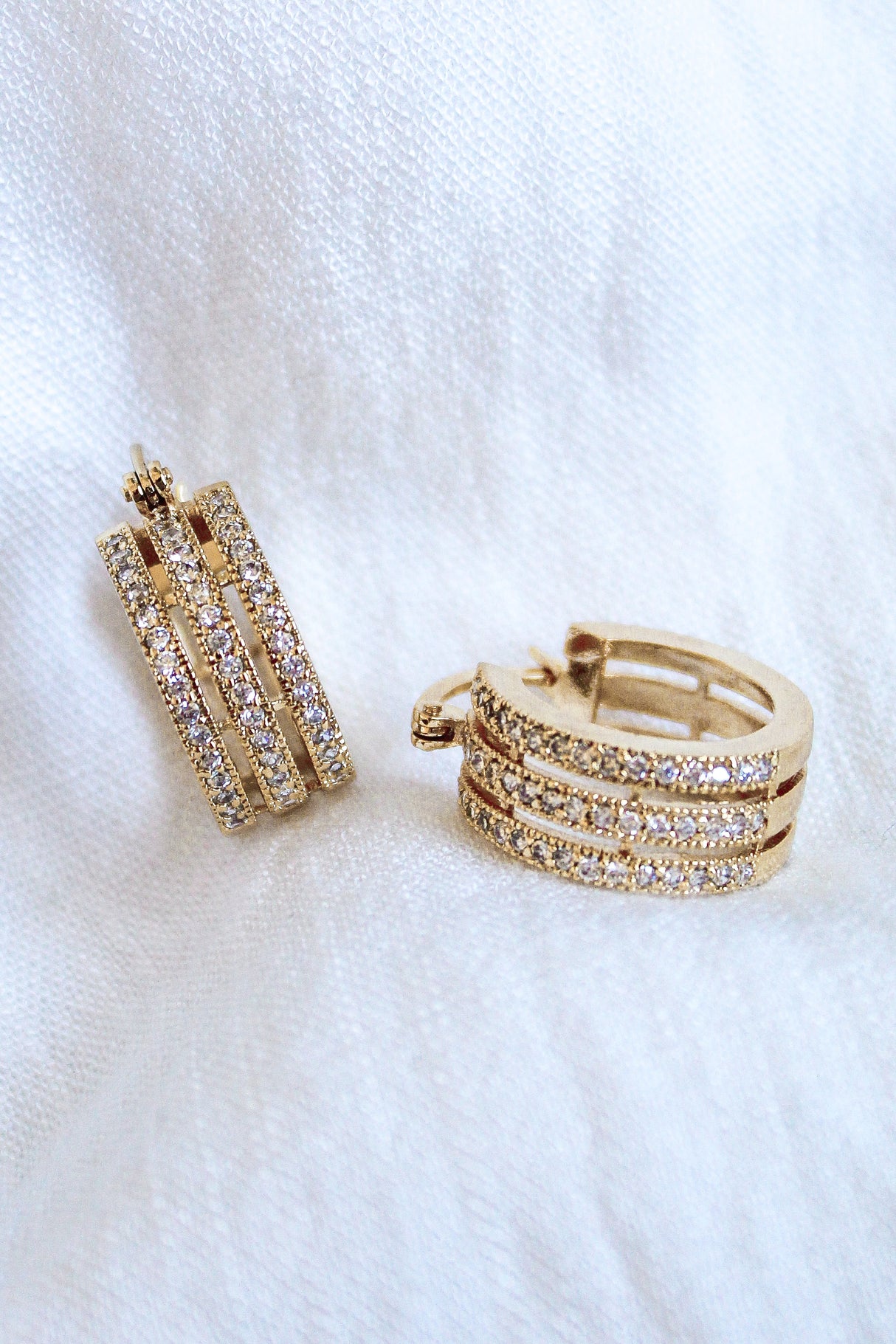 The Julia Triple Hoop by Kinsey Designs Archives features gold-filled hoops with three rows of sparkling Cubic Zirconia crystals, 1" diameter, showcased on a white fabric background.